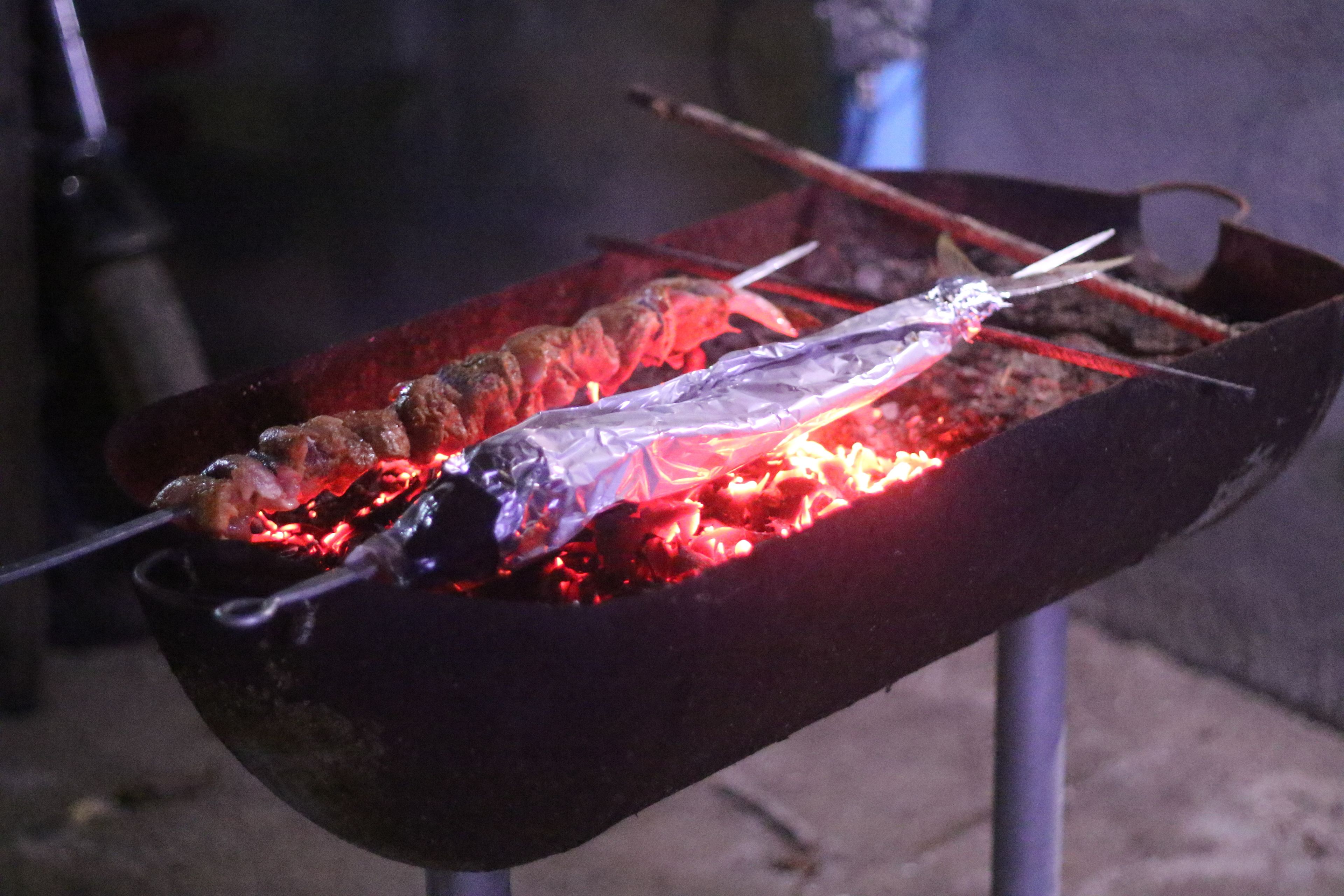 A grill with skewers of meat and foil-wrapped items cooking over charcoal.