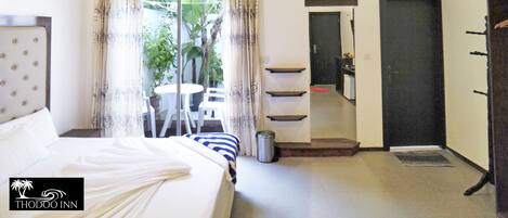 A hotel room with a bed, a small table with chairs, an air conditioning unit, a bathroom with a sink and mirror, and a door leading to another room.