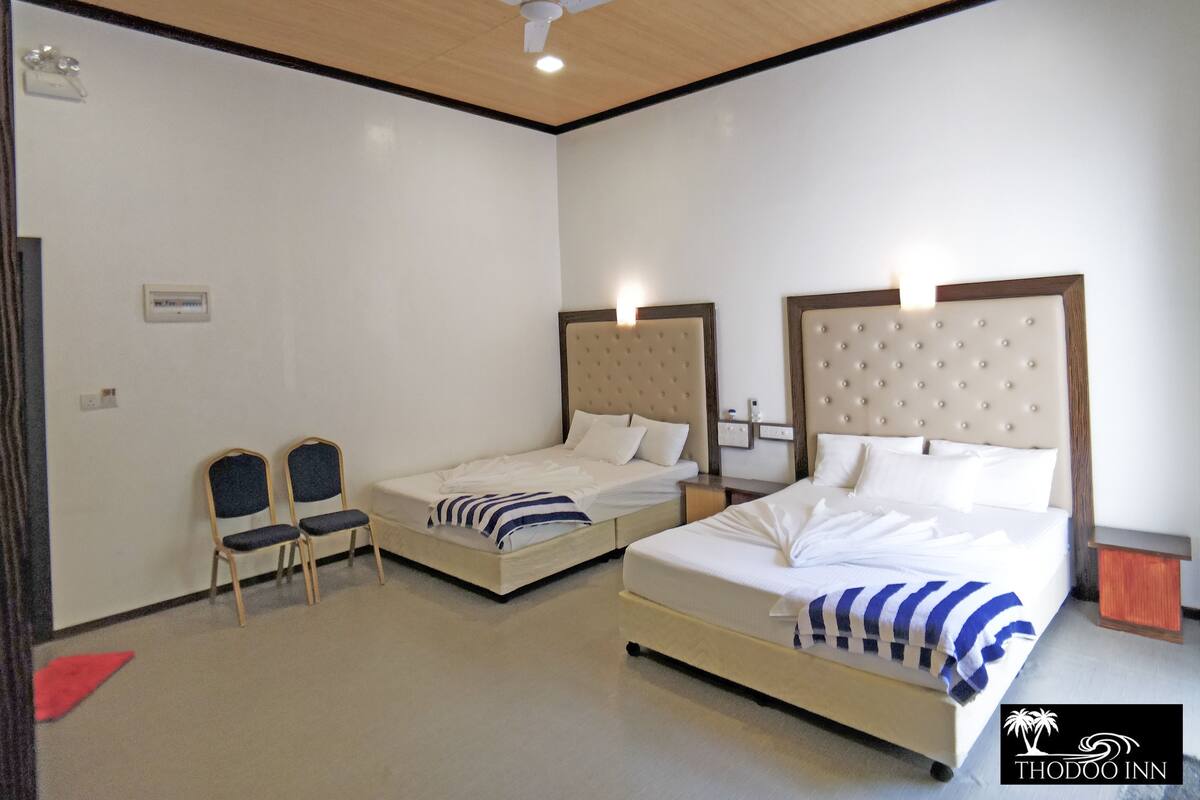 A hotel room with two beds, a ceiling fan, and a small seating area with chairs.