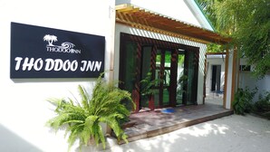 A THODOO INN sign, a wooden entrance with glass doors, and a small porch area with potted plants. - Thoddoo Inn (Thoddoo)