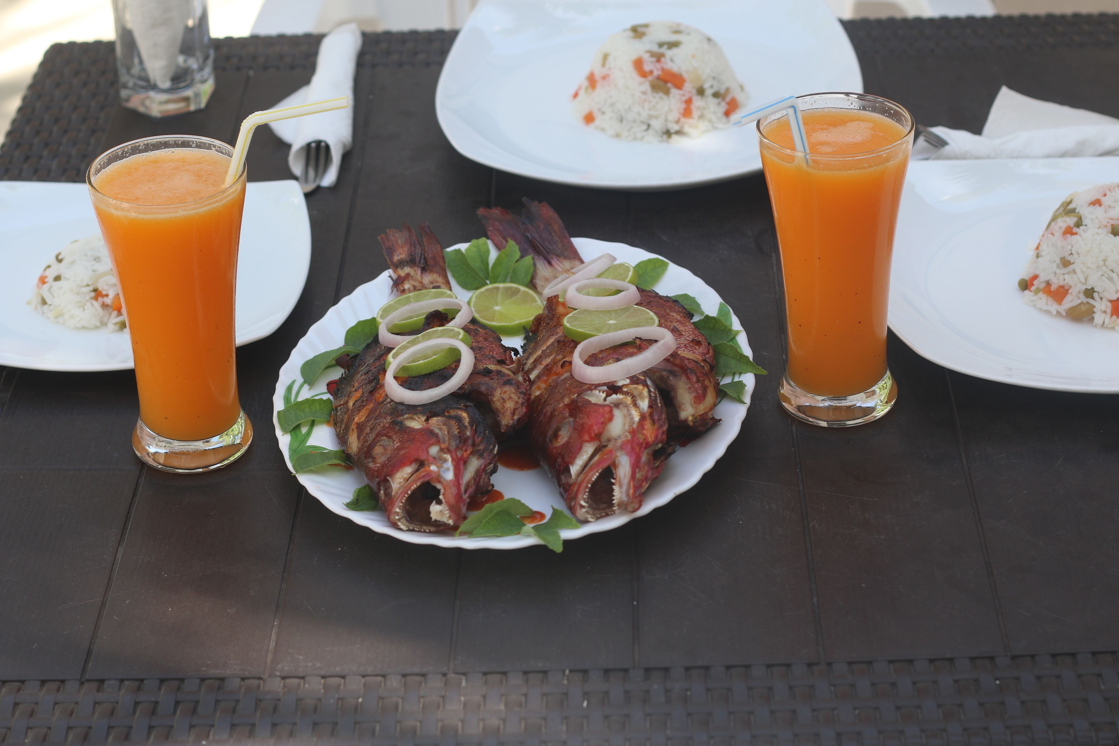 A table with a plate of grilled fish, two glasses of orange juice, and a plate of rice with vegetables.