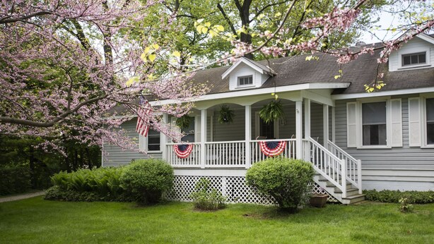 A two-story house with a porch, a small garden, and a flag.