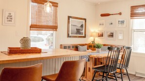 A kitchen with a wooden island, bar stools, a dining table with chairs, a hanging wooden paddle, and framed pictures on the wall.