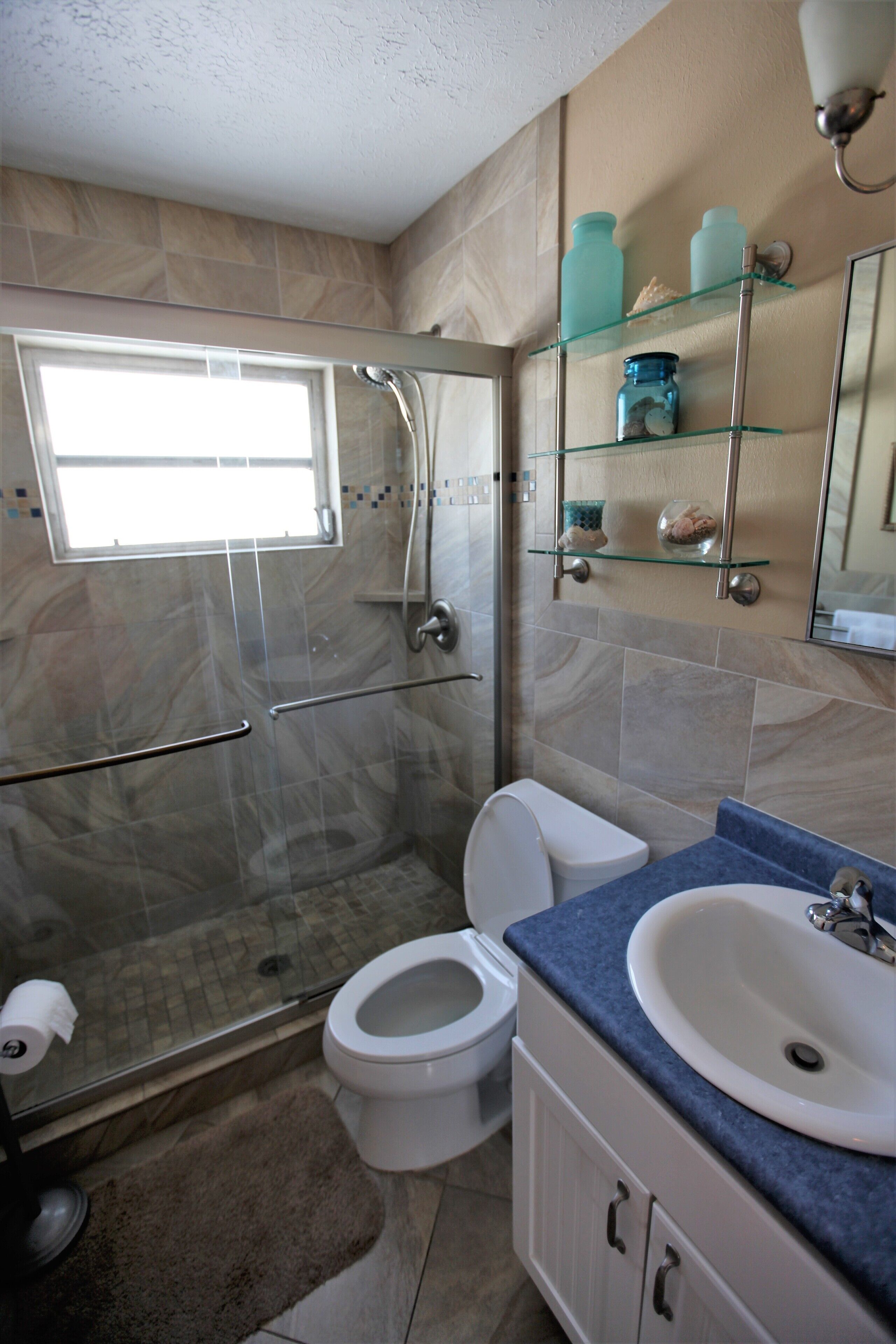 A bathroom with a glass shower enclosure, a toilet, a sink, and a mirror.