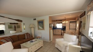 A living room with a brown sofa, a white sofa, and a glass coffee table. There is a kitchen in the background with a white refrigerator and a stove. - 1st Floor 2 Bed 1 bath home, short walk to beach, 1 step to door, North end LBK (Longboat Key)