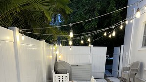 An outdoor patio with a white table and chairs, string lights, and a covered grill area. - 1st Floor 2 Bed 1 bath home, short walk to beach, 1 step to door, North end LBK (Longboat Key)