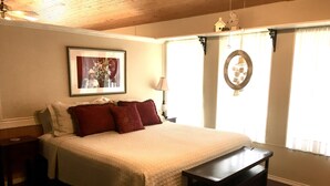 Un dormitorio con una cama grande, una mesita de noche, un aparador, un cuadro en la pared y una ventana con cortinas.