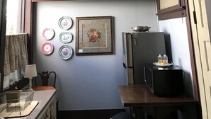 A small kitchen with a chandelier, a refrigerator, and decorative plates on the wall.
