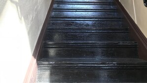 A black wooden staircase with a handrail, leading to a room with a chandelier.