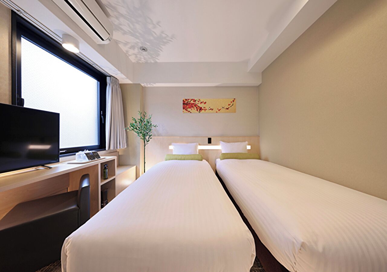Habitación de hotel con dos camas, un escritorio con televisor, una planta y un cuadro en la pared.