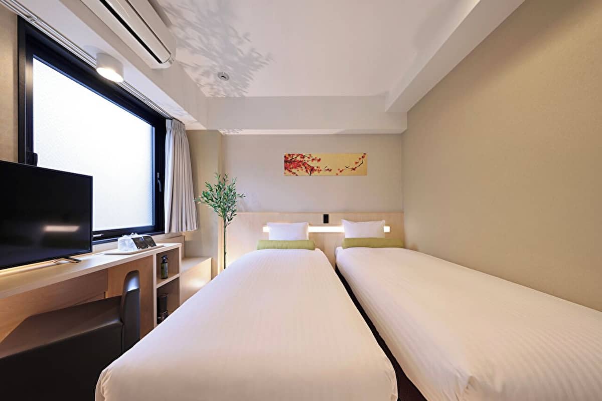 Een hotelkamer met twee bedden, een bureau met een televisie, een plant en een schilderij aan de muur.