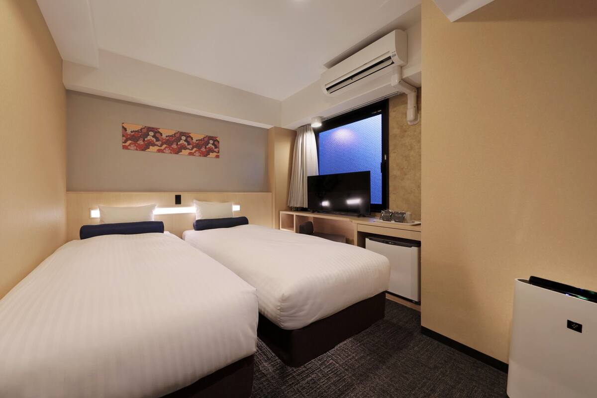 Een hotelkamer met twee bedden, een bureau met een computer, een televisie en een airconditioning.