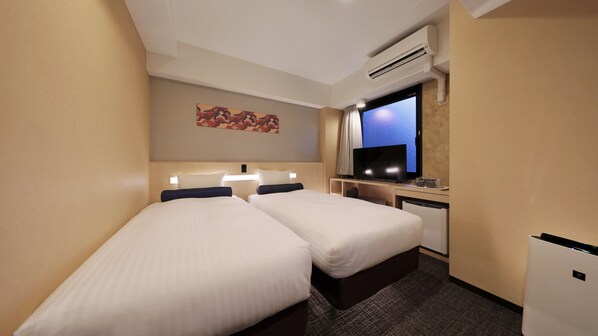 A hotel room with two beds, a desk with a computer, a television, and an air conditioning unit.