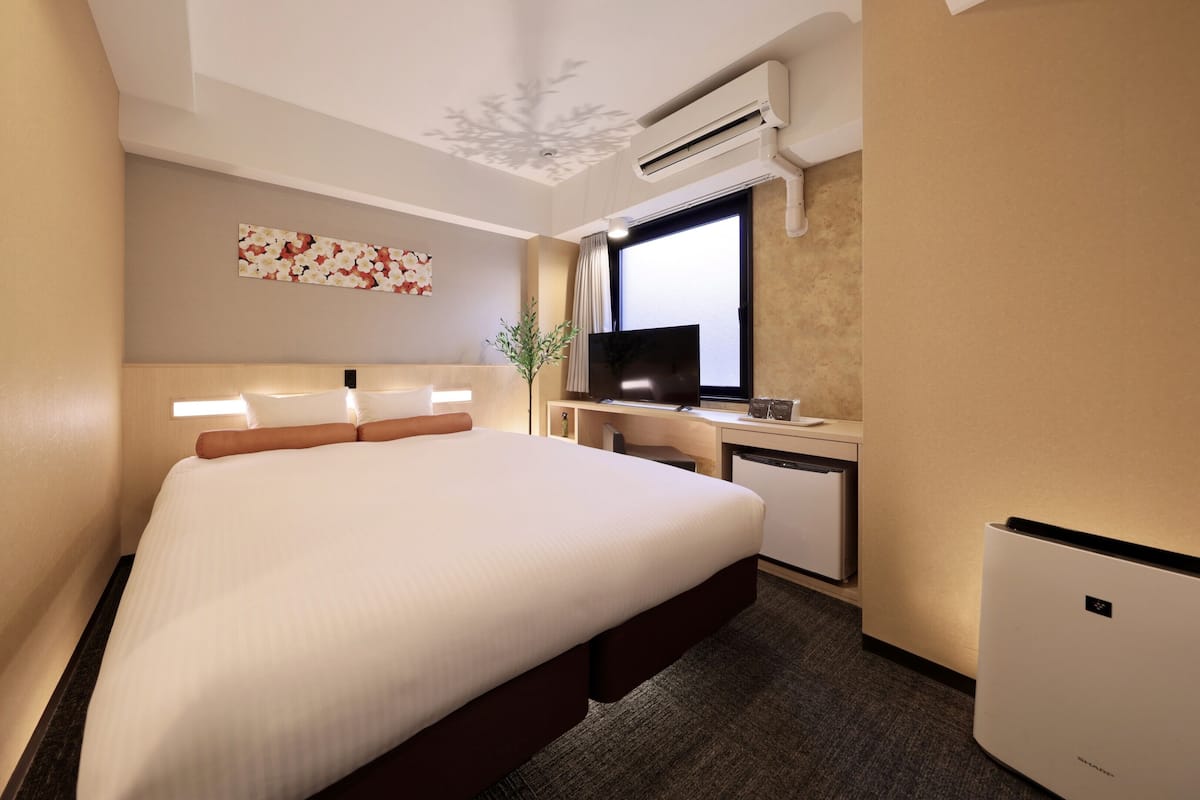 Een hotelkamer met een groot bed, een bureau met een televisie en een airconditioning.