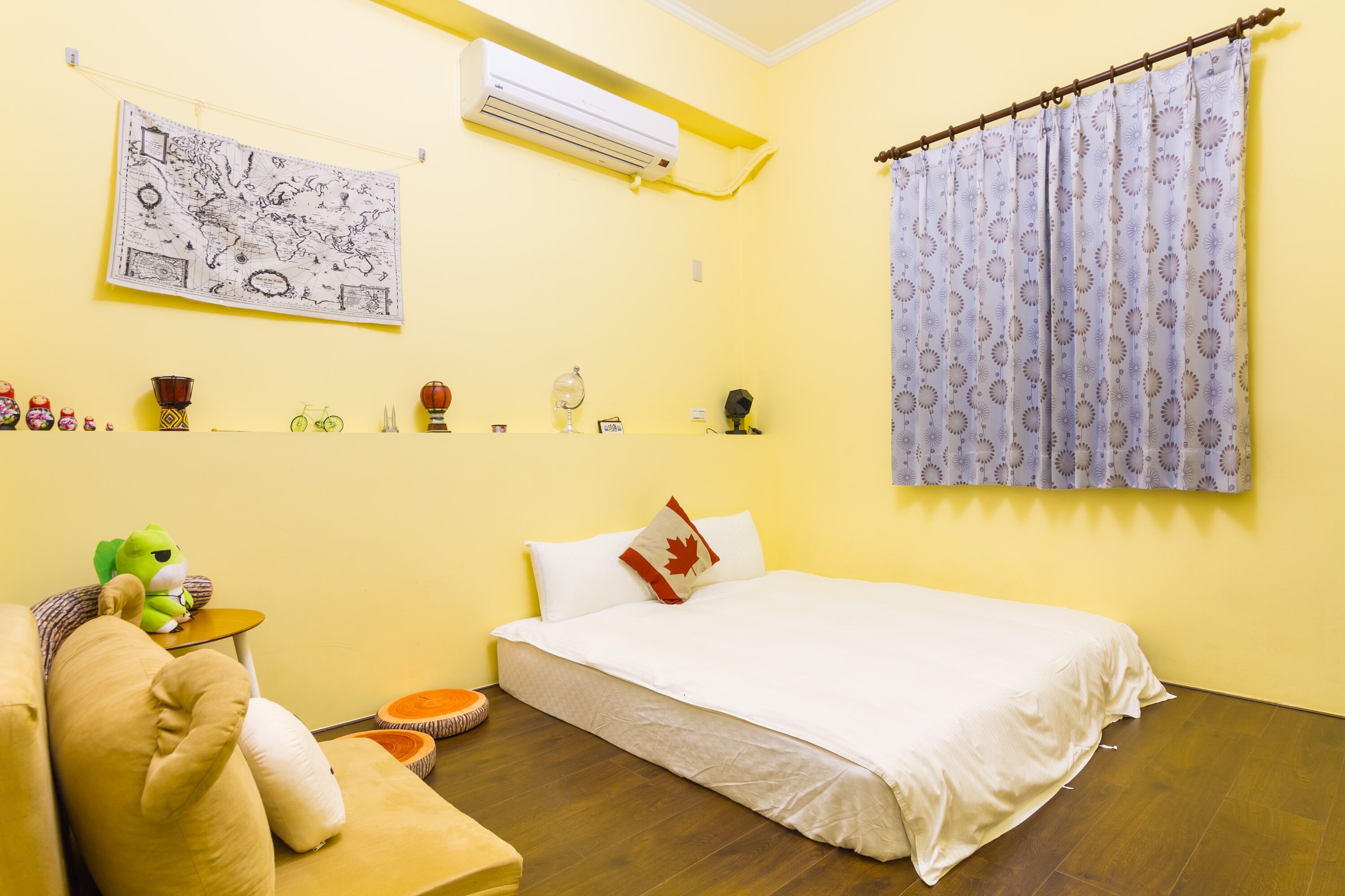 A room with a bed, a small table with a green toy, a map on the wall, and a curtain with a pattern.