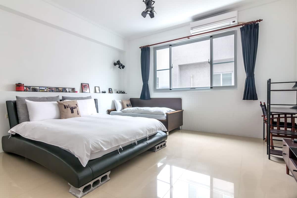 Un dormitorio moderno con una cama grande, una cama más pequeña, un escritorio y una ventana con cortinas.