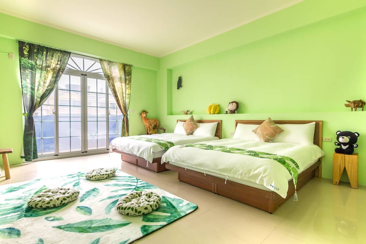Una habitación con dos camas, un ventanal con cortinas, una pared verde y un adorno con forma de oso.