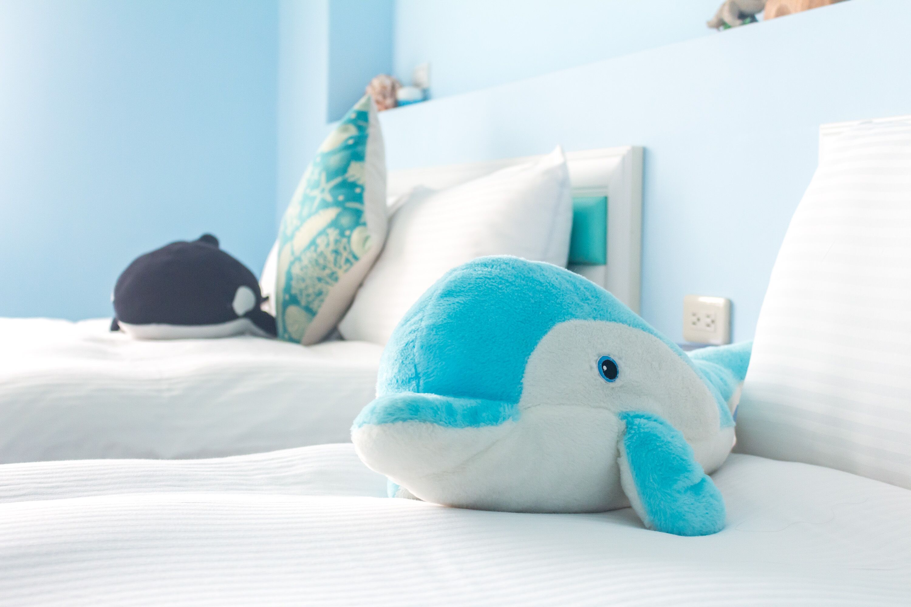 A bed with plush toys and pillows, a white wall, and a power outlet.