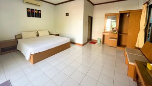 A hotel room with a large bed, a wooden wardrobe, a small desk, and a bathroom with a mirror and sink. - Sadudee Mansion (Surat Thani)