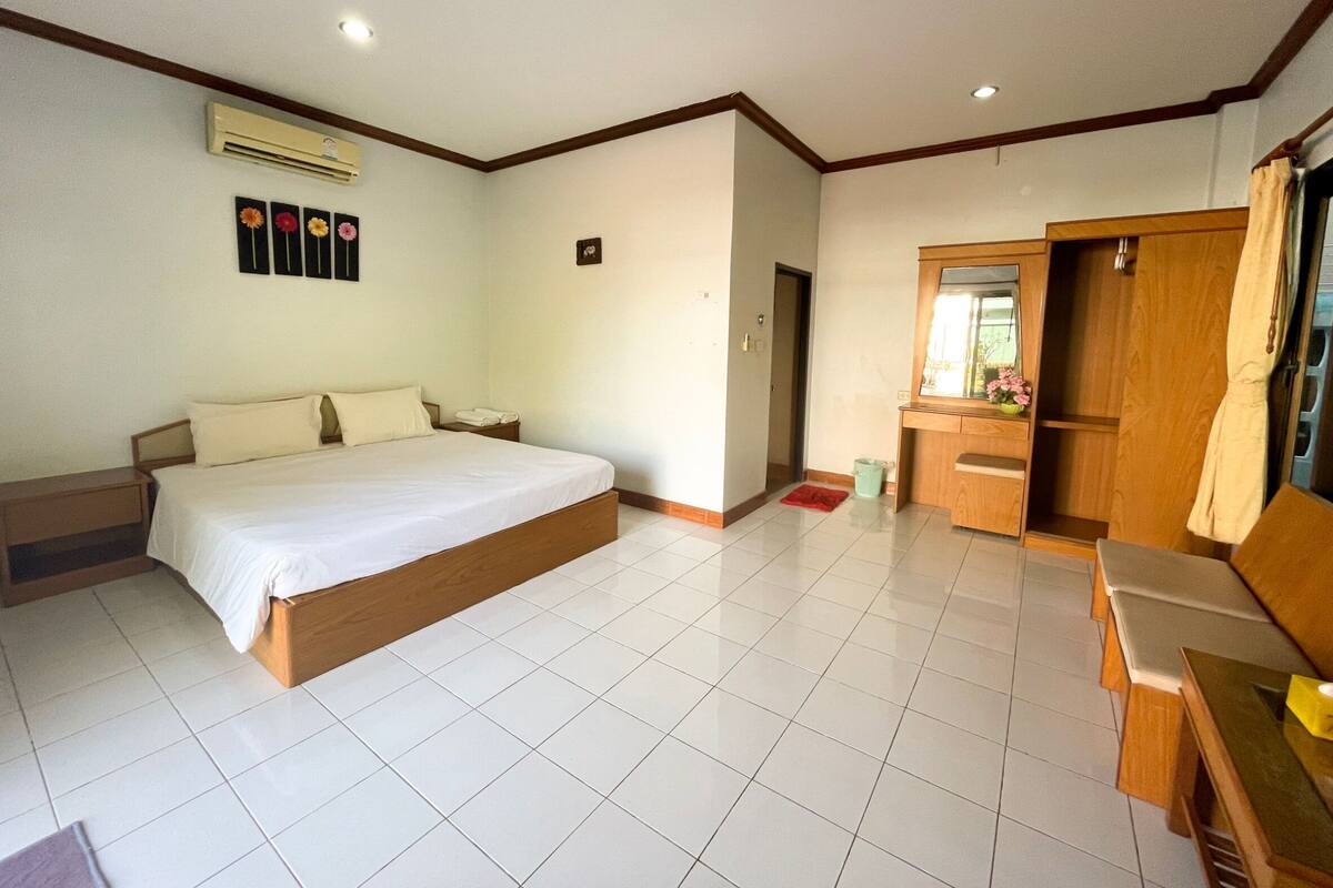 A hotel room with a large bed, a wooden wardrobe, a small desk, and a bathroom with a mirror and sink.