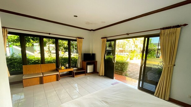 A spacious bedroom with a large bed, a TV, and a seating area by the window. - Sadudee Mansion (Surat Thani)