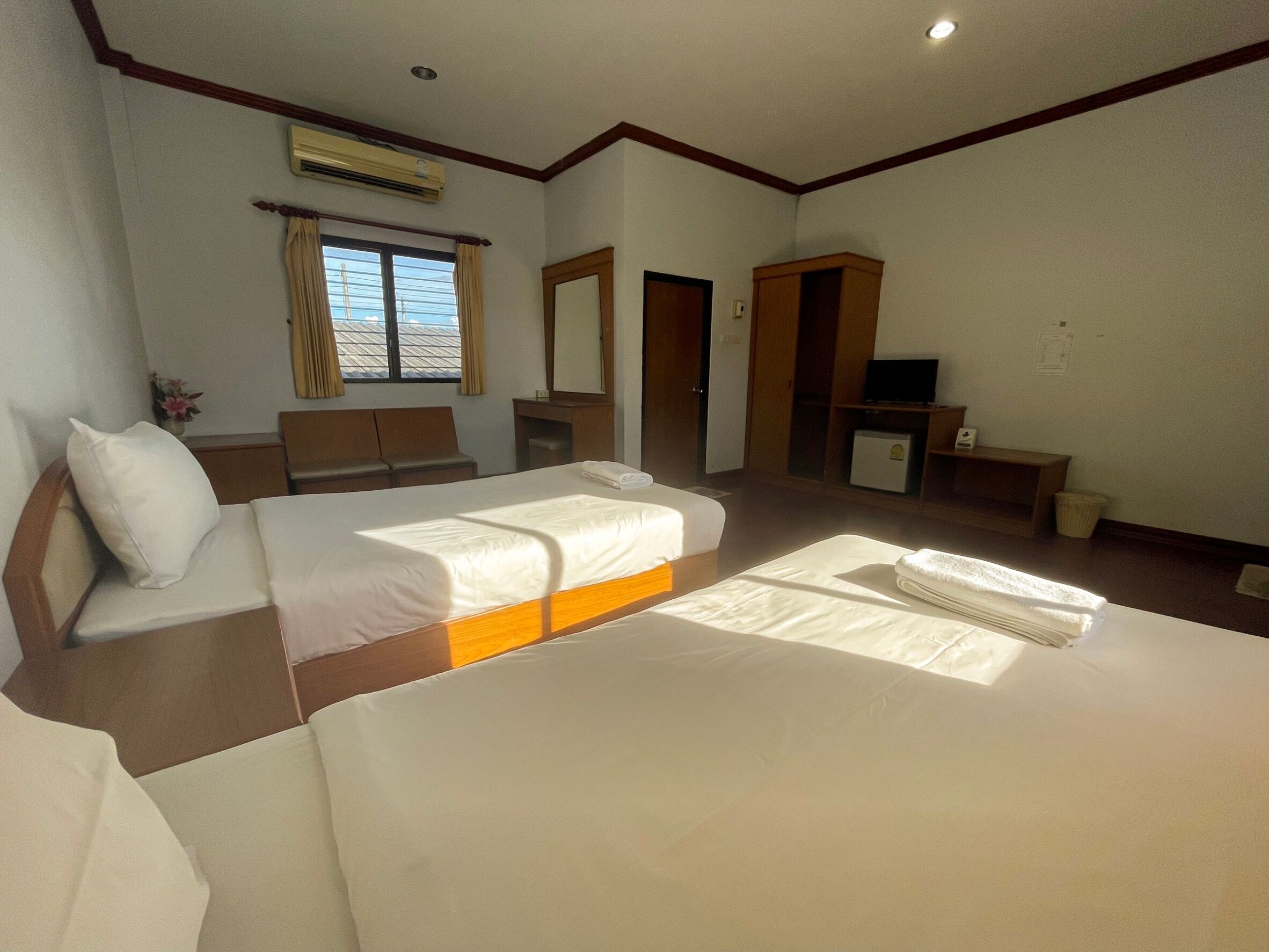 A hotel room with two beds, a desk, a TV, and an air conditioning unit.
