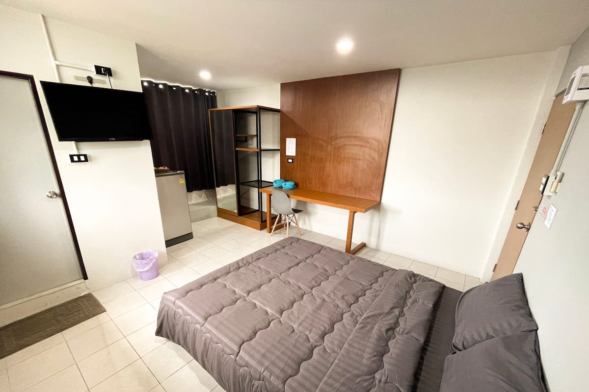A hotel room with a large bed, a desk, a wardrobe, and a shower area.