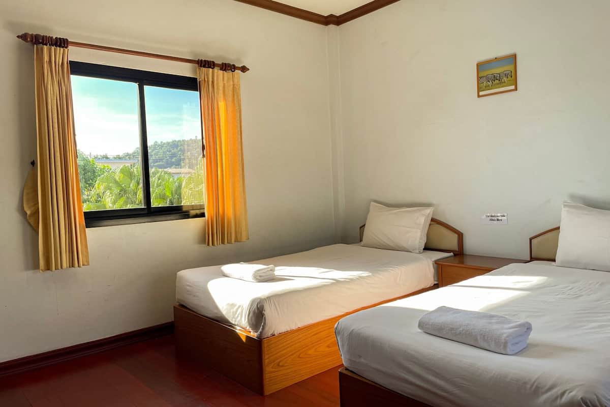 A room with two beds, a window with curtains, a small bedside table, and a wall-mounted picture.