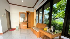 A modern room with a wooden bench, a small table with a kettle, and a view of greenery outside. - Sadudee Mansion (Surat Thani)