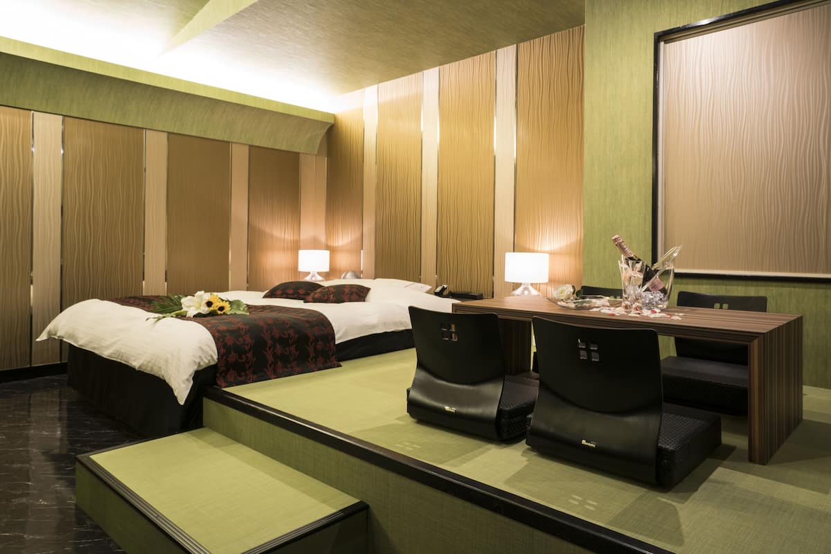 A hotel room with a bed, two bedside tables, a desk with chairs, and a large mirror.