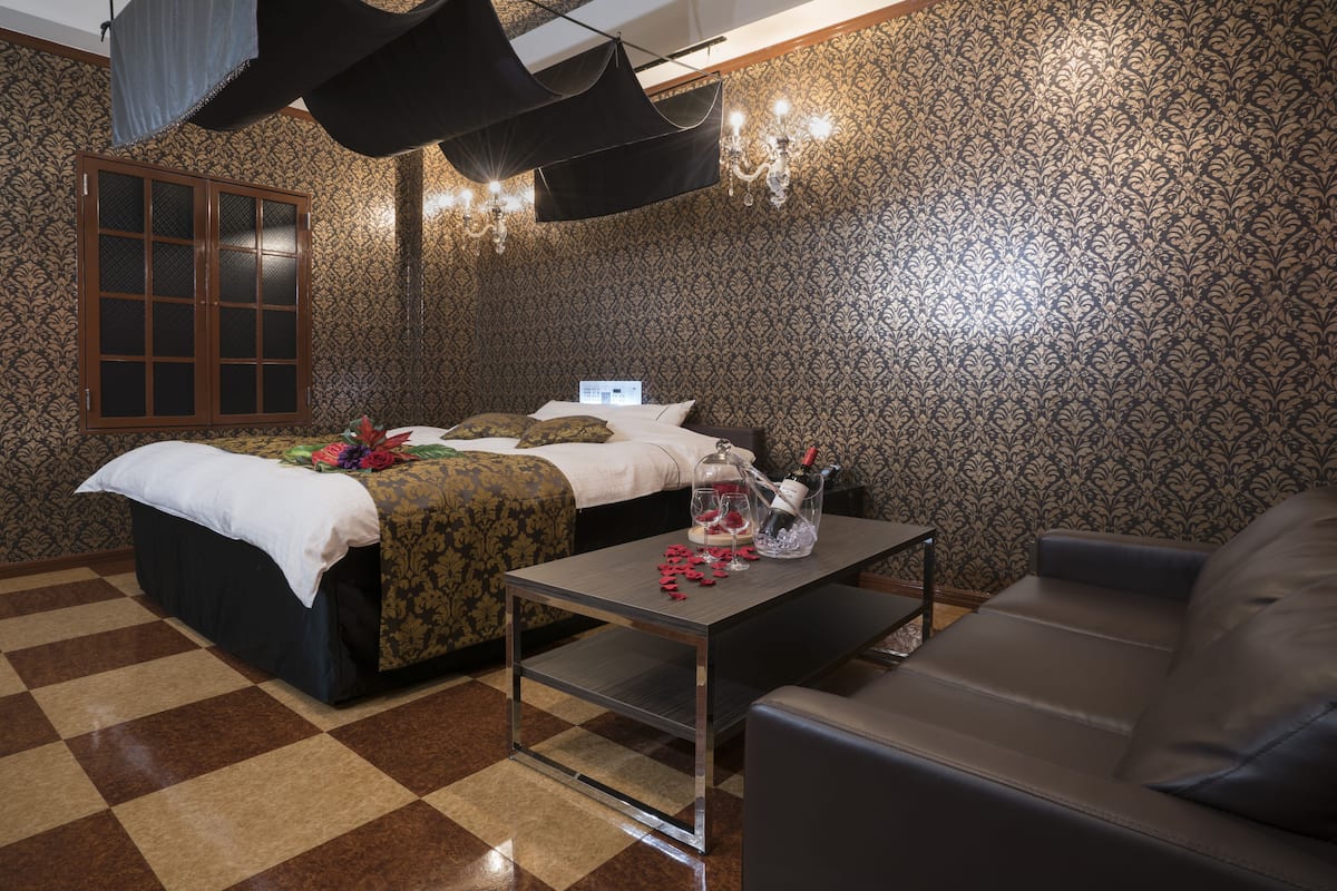 A bedroom with a bed, a sofa, a small table, and a chandelier.