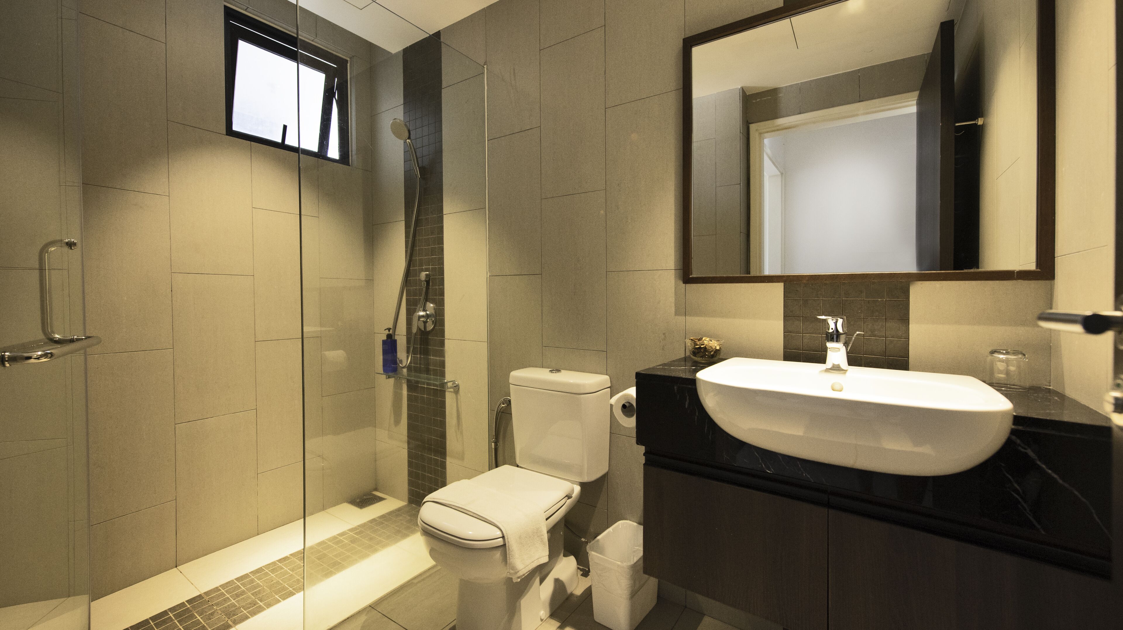 Et moderne badeværelse med en brusekabine med glasdøre, et hvidt toilet og en stor vask med en mørk bordplade.