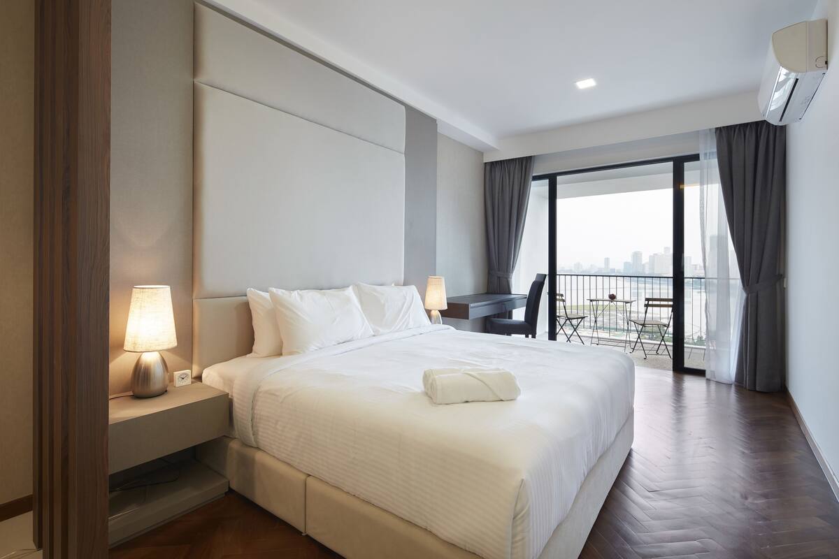 A hotel room with a large bed, a desk, and a view of the city skyline through a balcony.