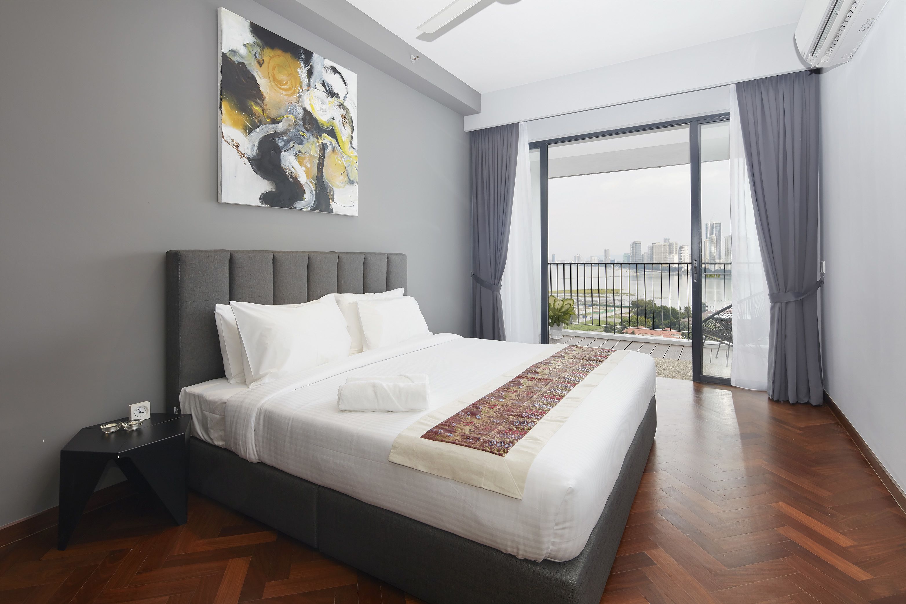 Een moderne slaapkamer met een groot bed, een nachtkastje, uitzicht op de stad door het raam en een schilderij aan de muur.