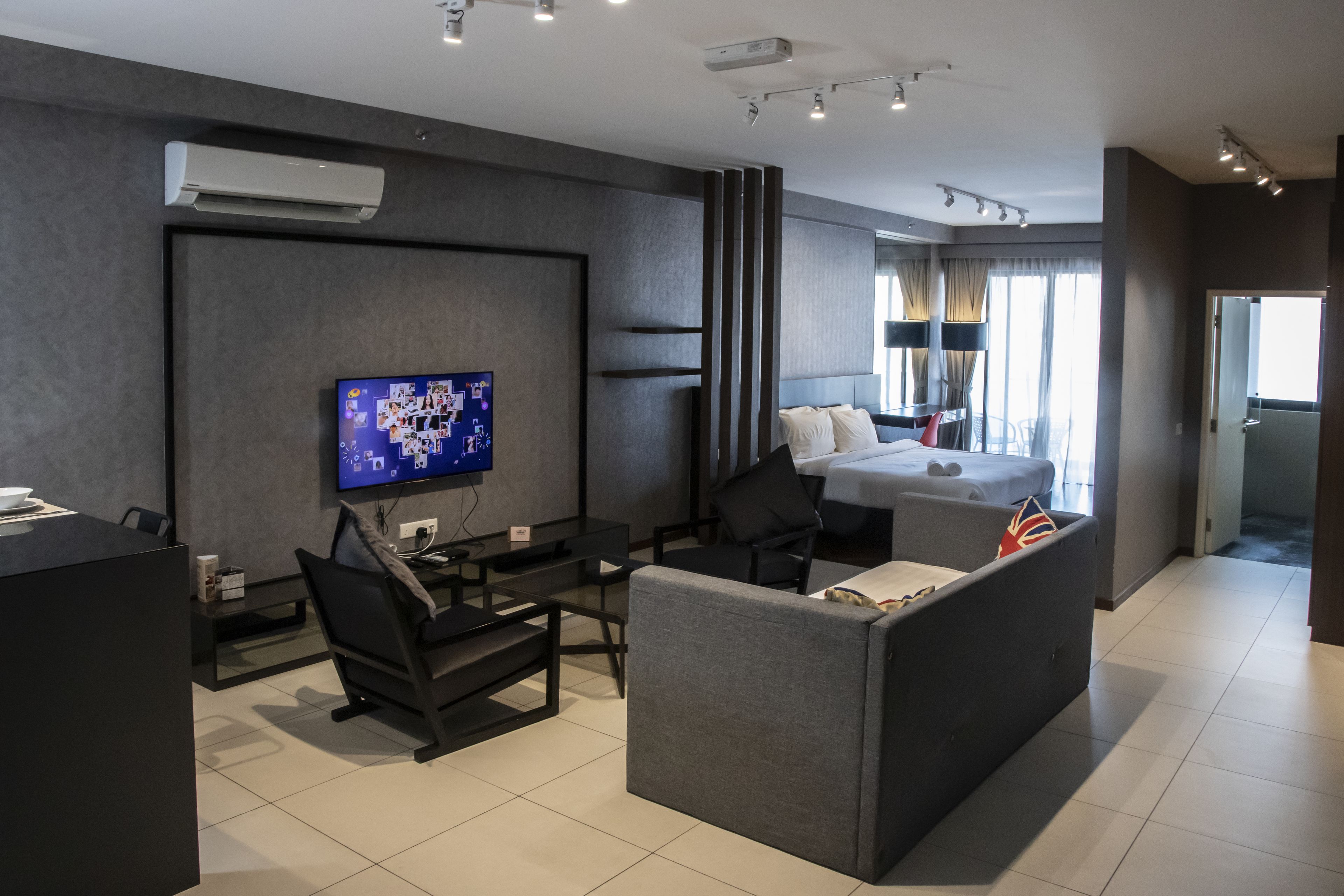 Une chambre d’hôtel moderne équipée d’une télévision à écran plat, d’un canapé, d’un lit avec des oreillers, d’un bureau avec une chaise et d’une fenêtre avec des rideaux.