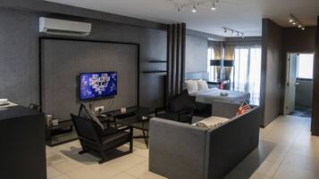 Una habitación de hotel moderna con televisión de pantalla plana, un sofá, una cama con almohadas, un escritorio con silla y una ventana con cortinas.