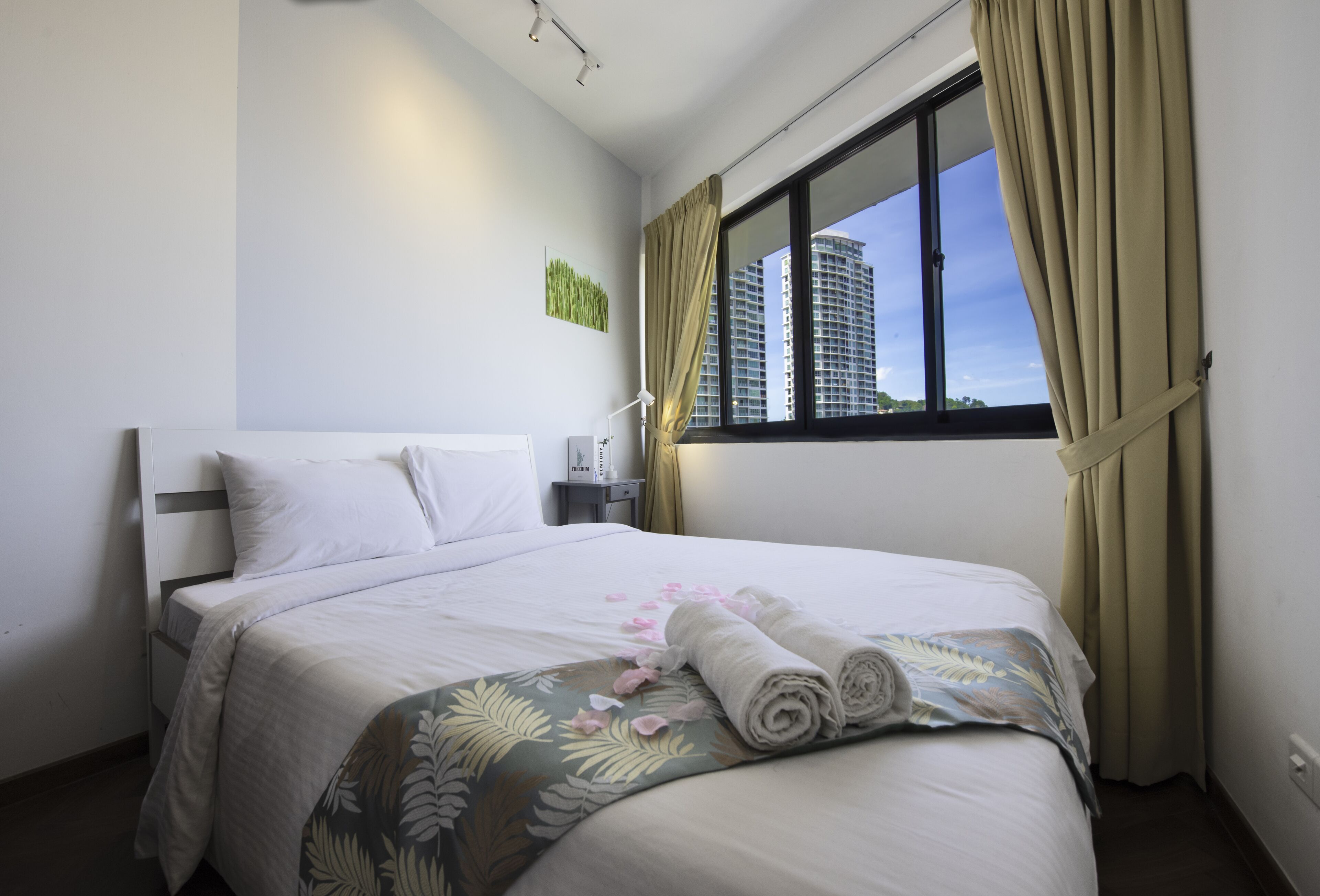A neatly made bed with white linens, a floral-patterned throw, and rolled towels.