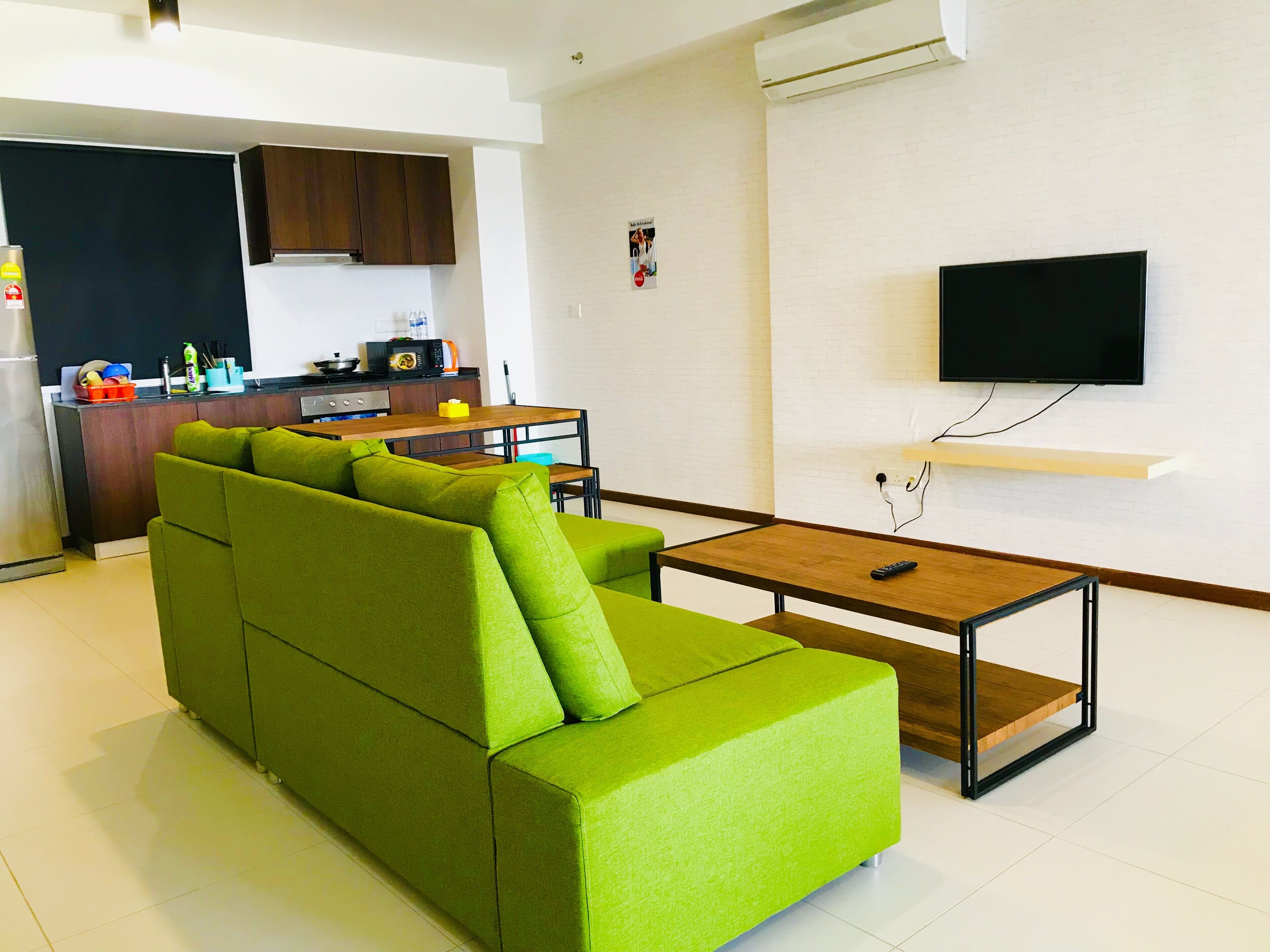 Una sala de estar moderna con un sofá seccional verde, una mesa de centro de madera y un televisor de pantalla plana montado en la pared.