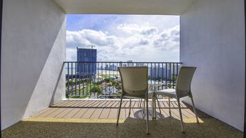 Varanda com duas cadeiras de vime e uma mesa pequena, com vista para paisagem urbana com edifícios e guindastes.
