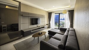 A modern living room with a sofa, a coffee table, a TV, and a view of a cityscape through large windows. - The Landmark by Katana (George Town)