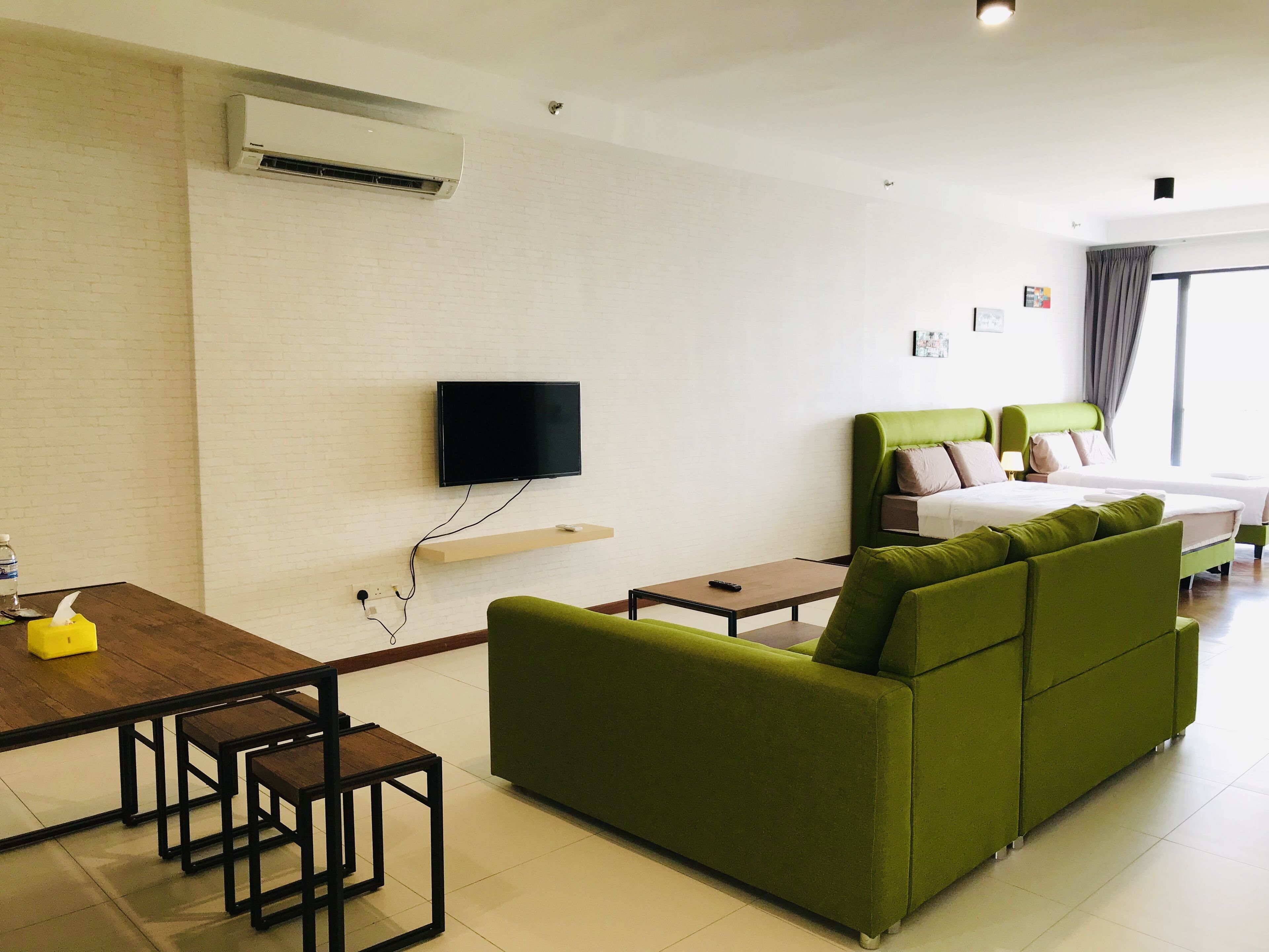 Een moderne hotelkamer met een groene bank, een bed met een groene hoofdbord, een flatscreen-tv aan de muur, een houten tafel met stoelen en een klein tafeltje met een afstandsbediening.