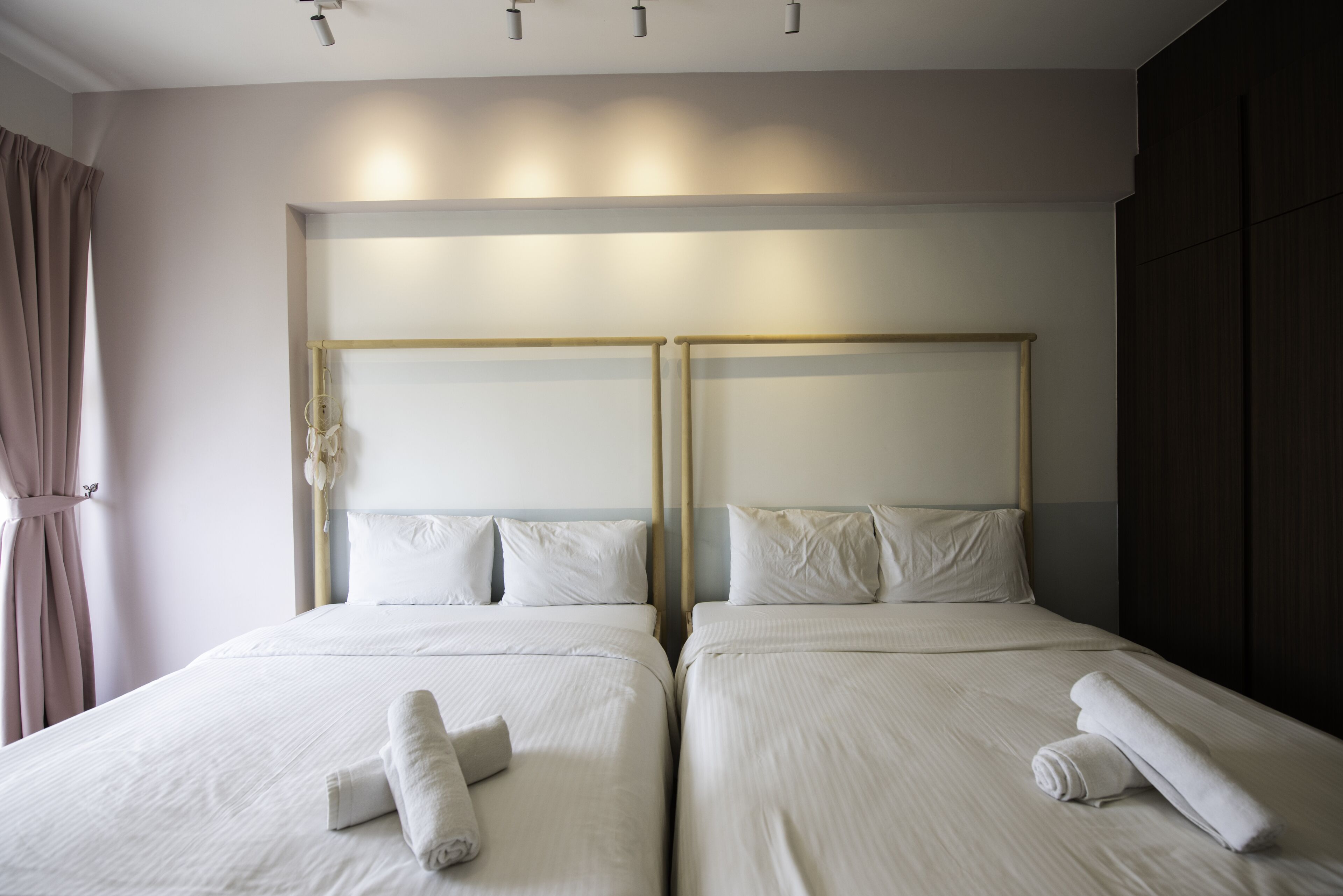 Habitación de hotel con dos camas, cada una con cabecero de madera, ropa de cama blanca y toallas enrolladas sobre las camas.