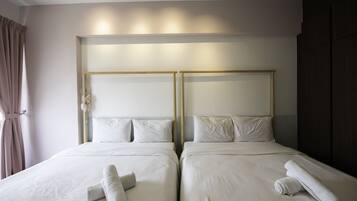 Habitación de hotel con dos camas, cada una con cabecero de madera, ropa de cama blanca y toallas enrolladas sobre las camas.