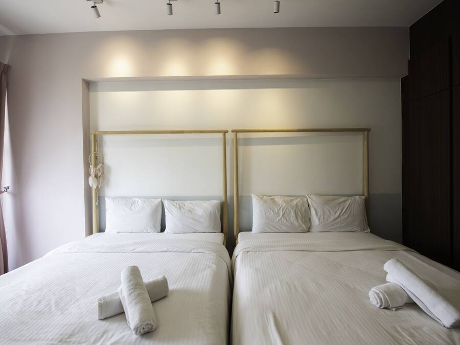 Habitación de hotel con dos camas, cada una con cabecero de madera, ropa de cama blanca y toallas enrolladas sobre las camas.
