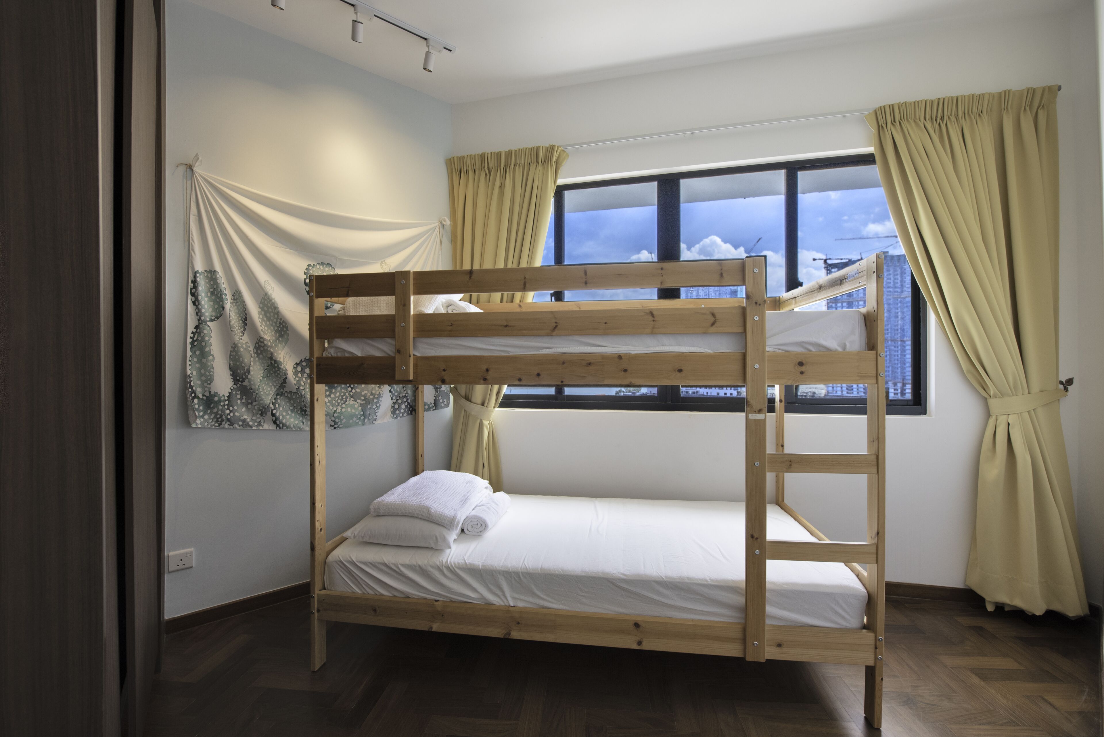 A bunk bed room with a window, curtains, and a patterned wall hanging.