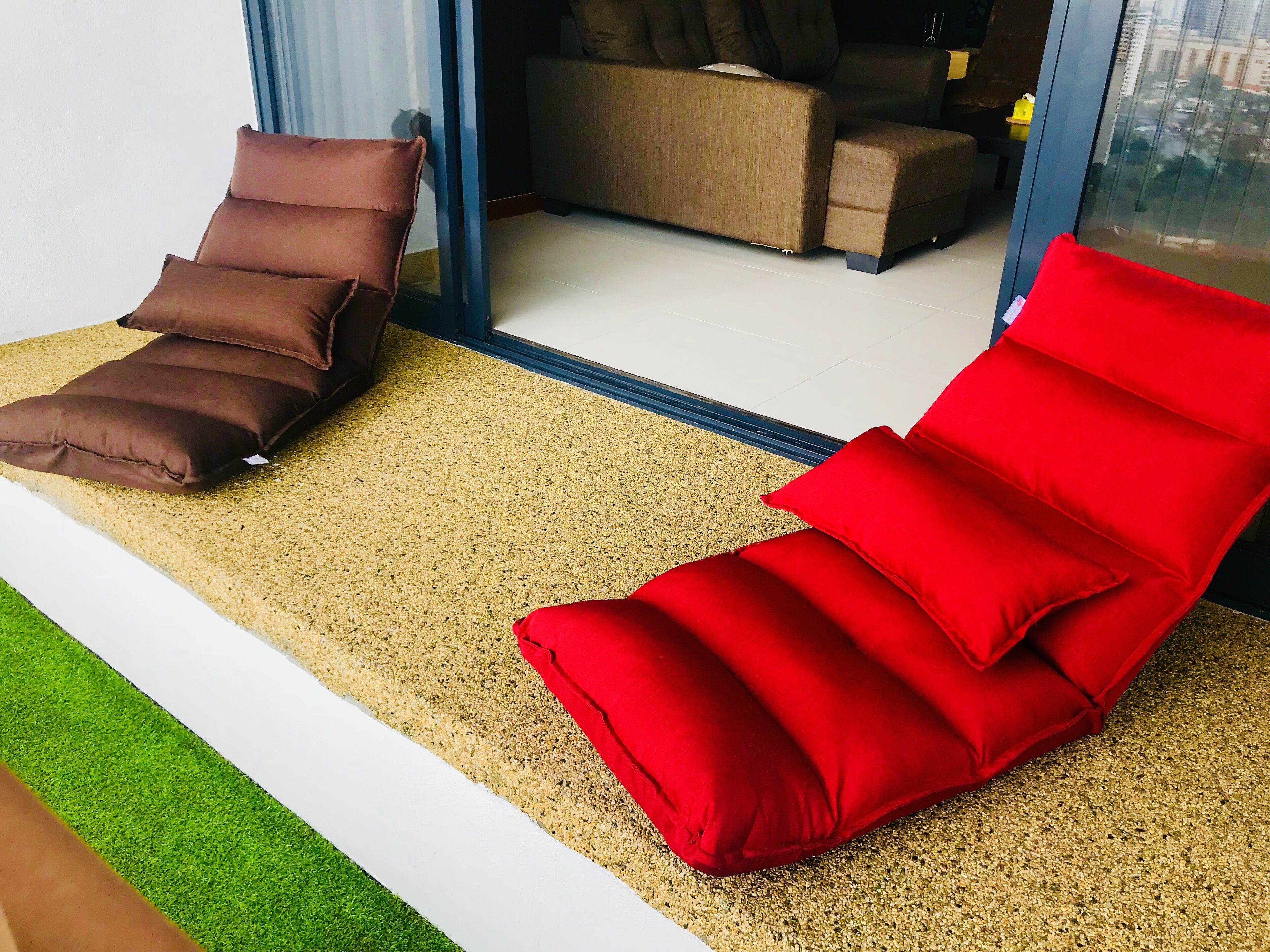A room with a sofa and two cushions, a window, and a view of the outside.
