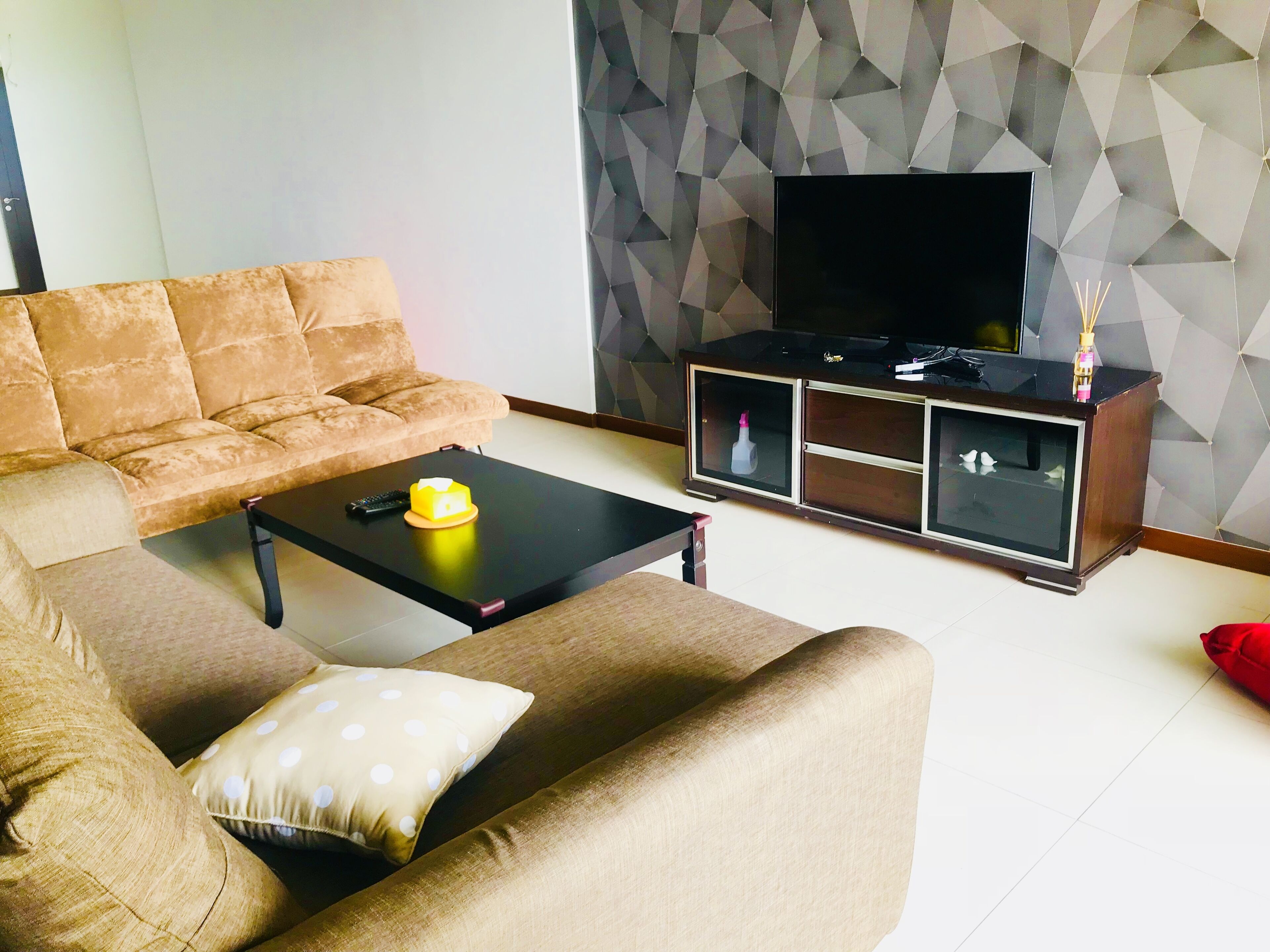 Un salon comprenant un canapé, une table basse, un meuble pour la télévision et un mur orné d’un motif géométrique.