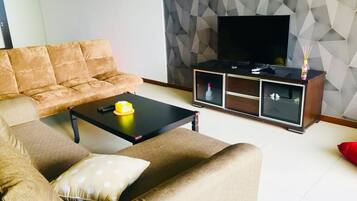 Un salon comprenant un canapé, une table basse, un meuble pour la télévision et un mur orné d’un motif géométrique.