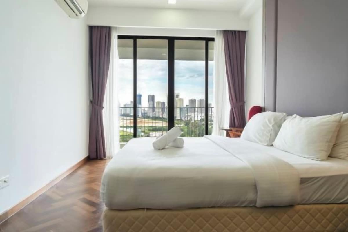 A hotel room with a large bed, a city view through a sliding door, and a wooden floor.
