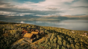Conjunto de cabañas con varias construcciones, rodeado de un bosque denso y con vistas a una amplia masa de agua.